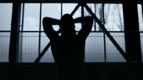 slim dancer silhouette raising hands in dark studio. unknown woman dancing class