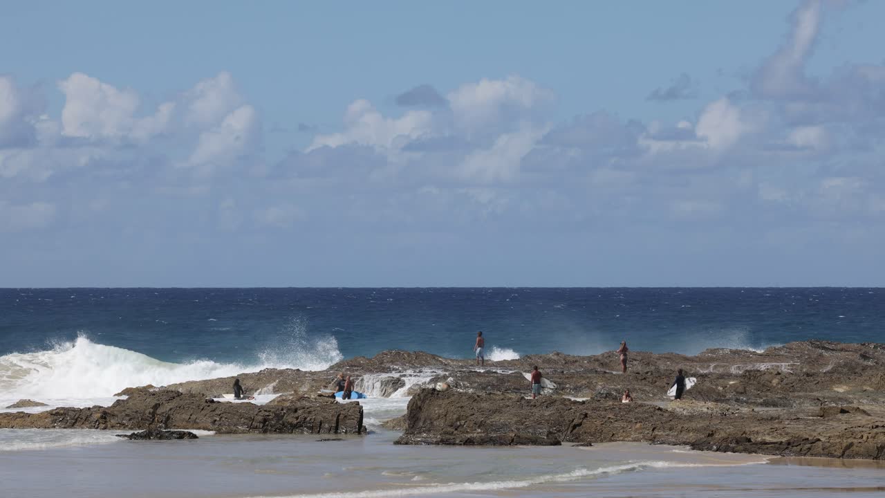 바위 가 있는 해변 에서 바다 파도 를 즐기는 사람 들