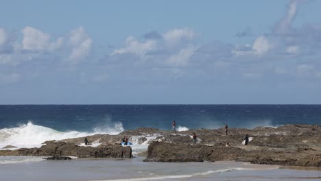 personas disfrutando de las olas del océano en una orilla rocosa