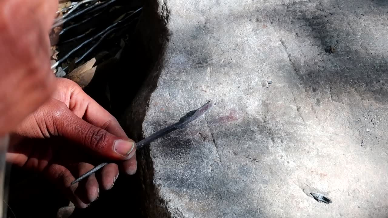 primer plano de un hombre africano que da forma a un trozo de metal con un martillo para crear una punta de flecha