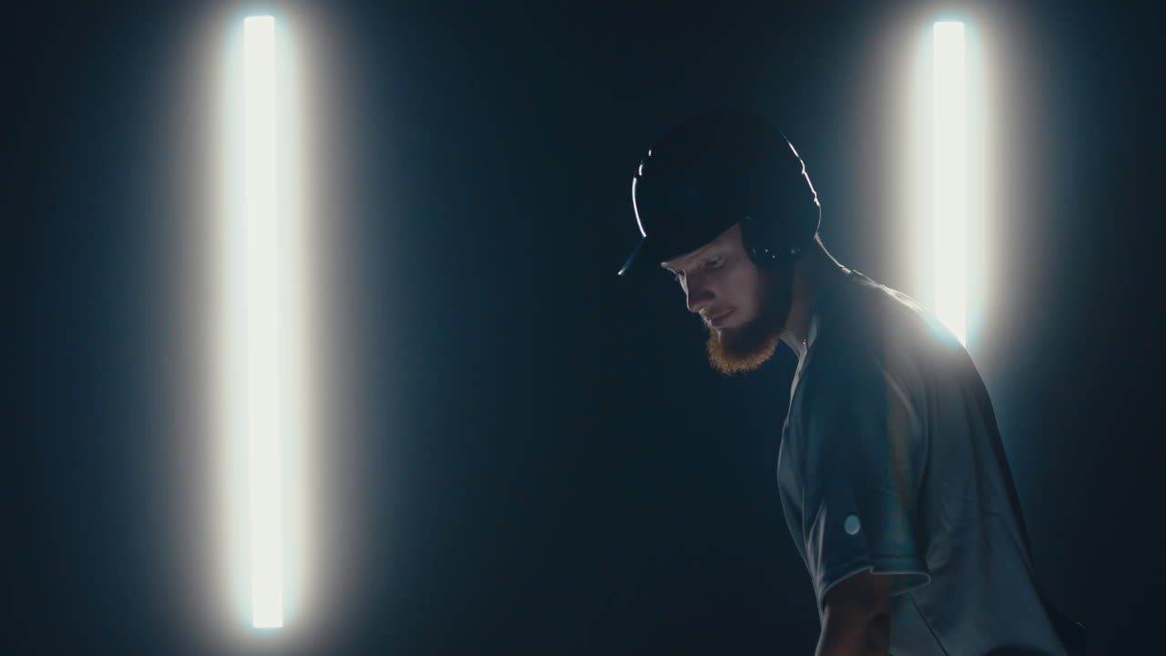 jugador de béisbol profesional caucásico posando contra un fondo oscuro. 4k uhd 60 fps cámara lenta