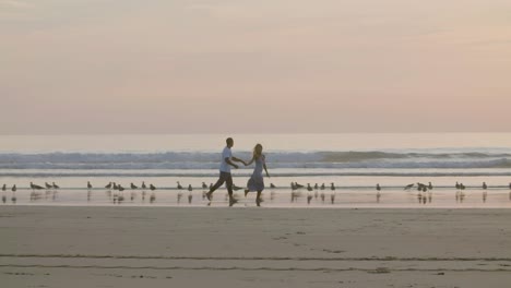 romantic caucasian couple running along beach, holding hands.