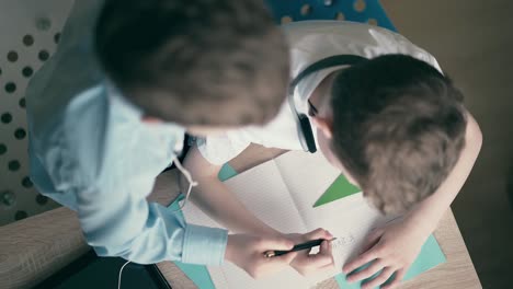 High-angle-shot-Children-little-boys-do-school-homework-sitting-at-a-table-in-a-notebook-thinking