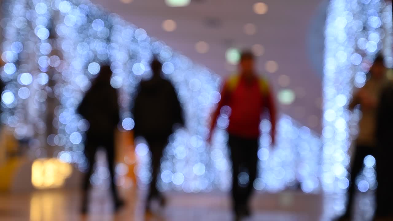 Blurred view of people walking through a shopping mall with Christmas lights on the walls