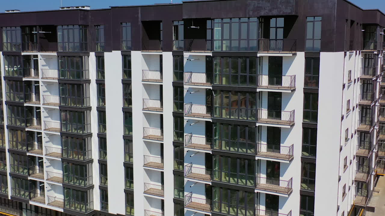 Facade of new block of flats. Modern design of black and white multi storey architecture in the city. Beautiful high-raise building with balconies and tall windows.