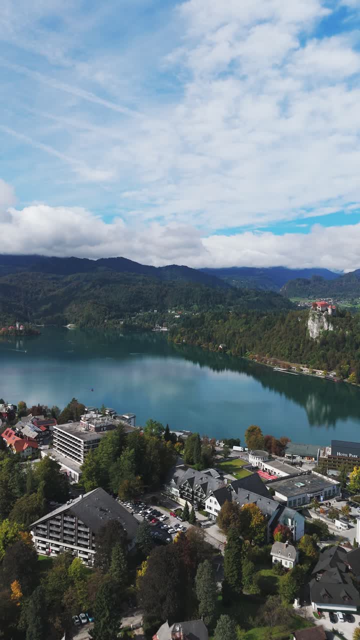 Vista aerea del lago di Bled con la città in riva al lago, le colline boscose e il castello di Bled sulla scogliera rocciosa sotto il cielo nuvoloso