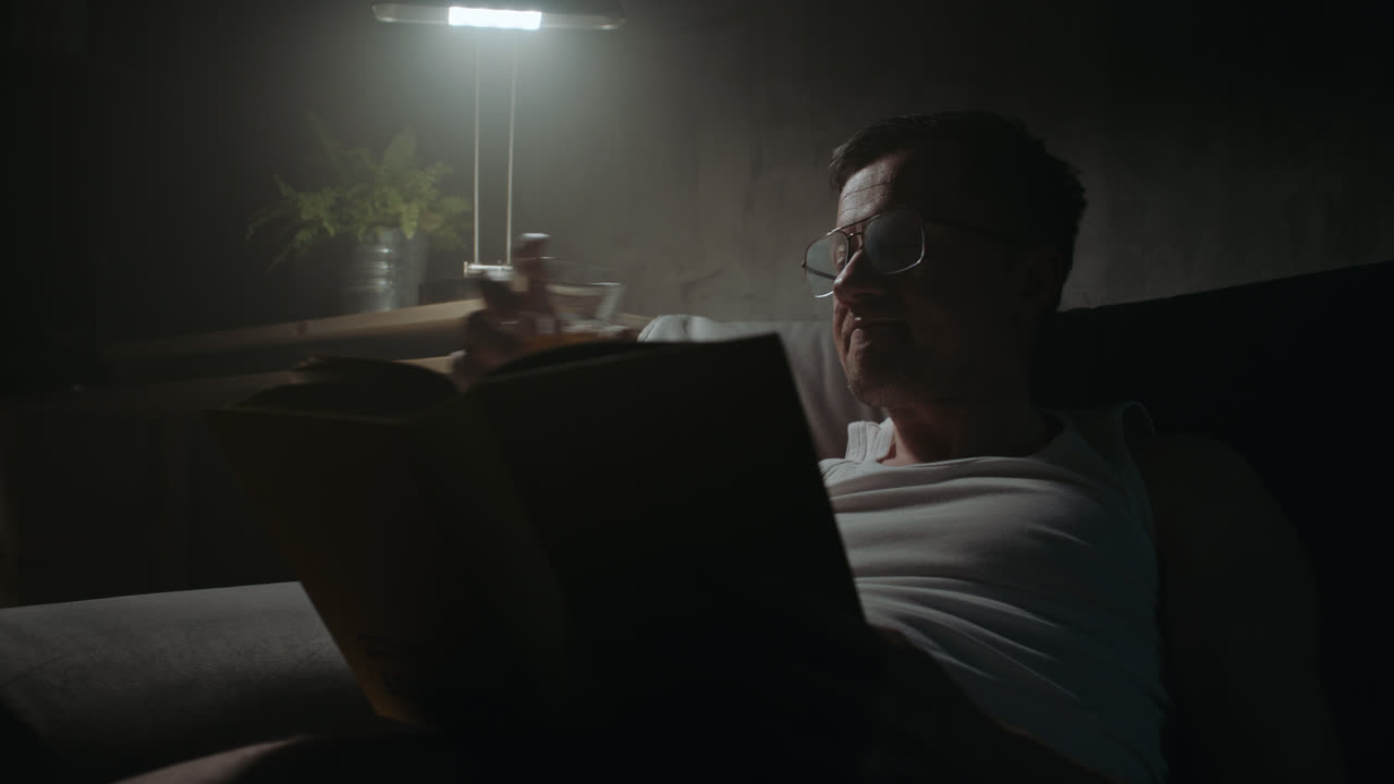 A sad man reads a book at night in his underwear