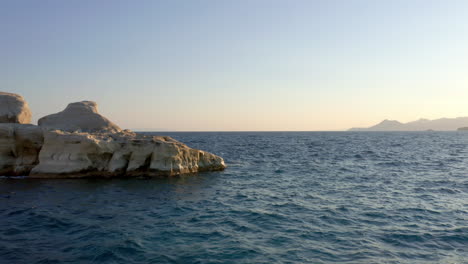 Vista-Aérea:-Volando-Hacia-Atrás-Y-A-Baja-Altura-En-La-Playa-Sarakiniko-De-La-Isla-De-Milos,-Cícladas,-Grecia,-Durante-El-Amanecer