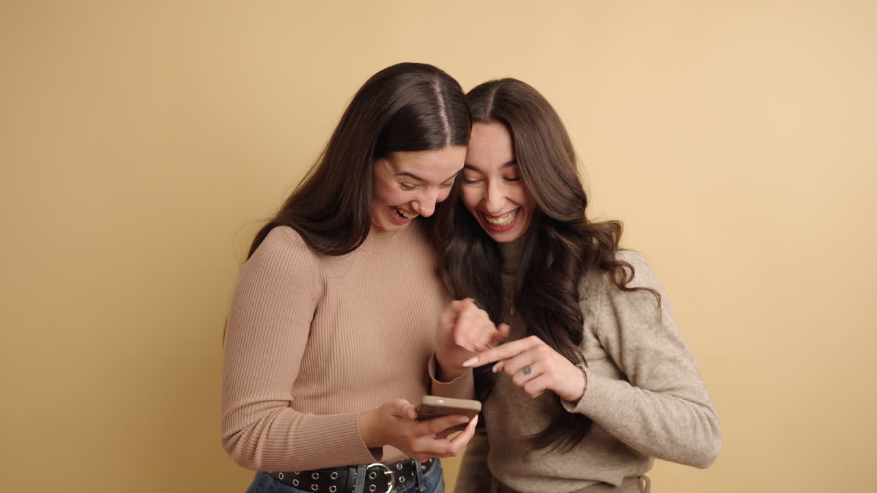 Two young women laughing and pointing at smartphone screen