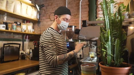 barista wearing facemask while making hot coffee drink inside a coffe shop. - medium shot
