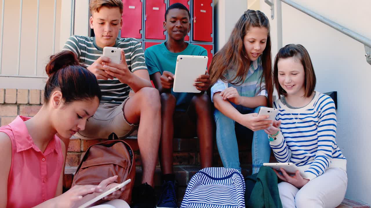 Gruppo di studenti sorridenti sulle scale che usano uno smartphone e un tablet.