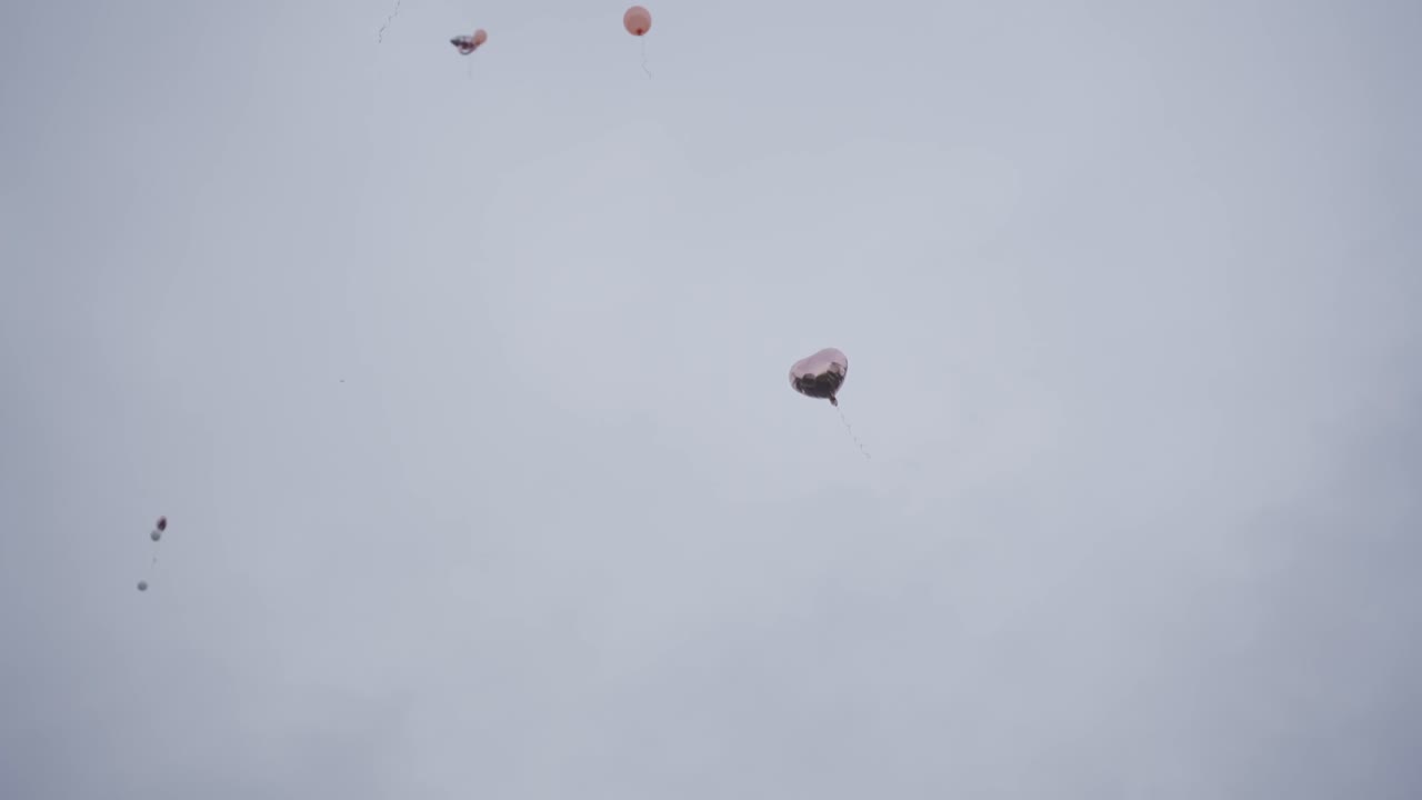 은색 하트 풍선은 집을 지나 하늘로 천천히 날아갑니다. 배경에서 더 많은 풍선을 볼 수 있습니다.