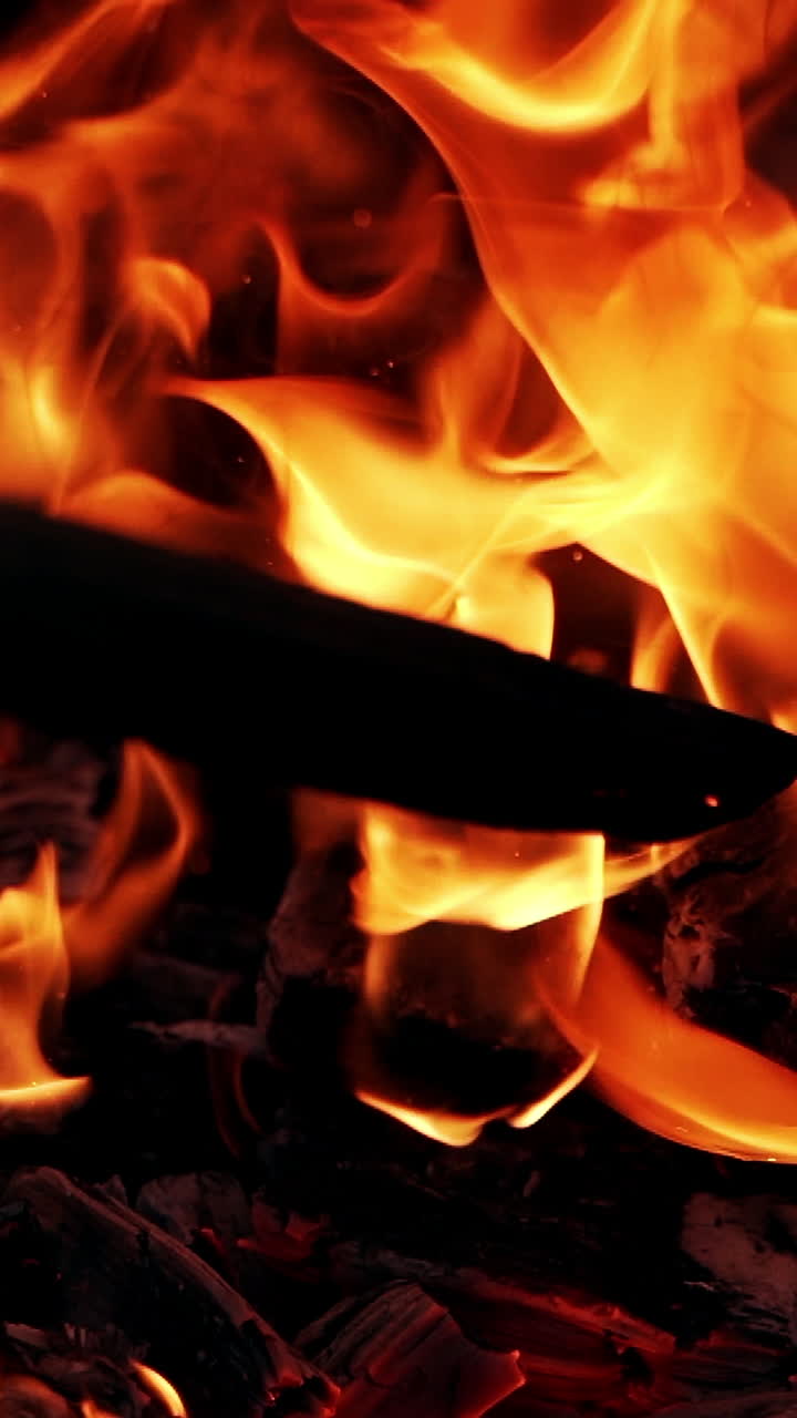 Bright fire motion. Sparkles of red and yellow flame from smoldered logs. Wooden stick beats a black log in the burning fire. Slow motion. Vertical video