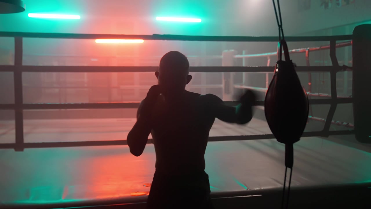 Silhuet af en bokser, der træner med en speedbag i et mørkt træningscenter med neonlys