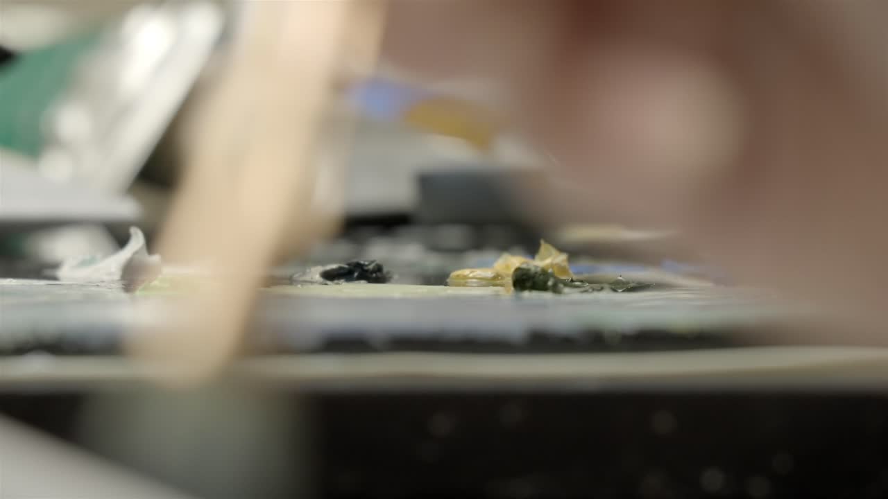 Close up of artist hands mixing oil paint on palette in art studio