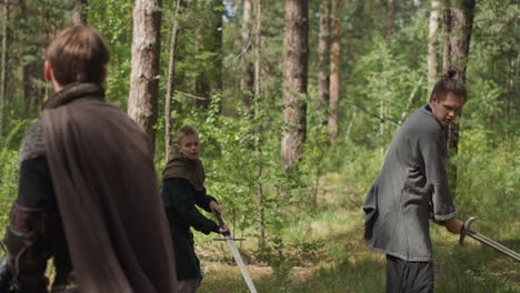 teenage boys train sword strikes with master in pine wood