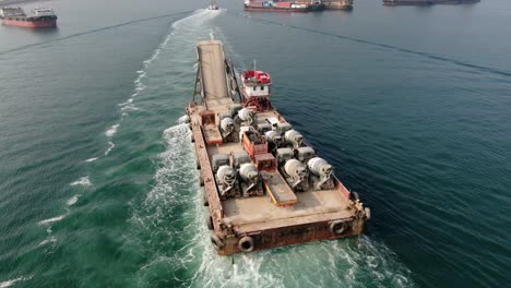 barge loaded with concrete mixer trucks pulled to port by a tugboat in hong kong bay, aerial view