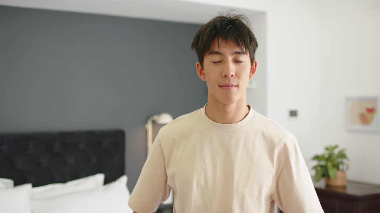 Accorgendosi della telecamera, un uomo asiatico sulla ventina si raddrizza, si gira, si avvicina e sorride accanto a una lampada da comodino.