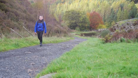 a young boy, with backpack camera and tripod in hand, walking through a tranquil autumn-winter woodland with a meandering stream