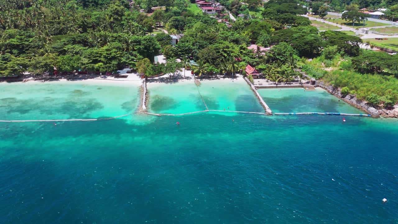 Drone view of a tropical beach with enclosed swim zones, turquoise waters, and white sand backed by lush greenery—great for travel, resort, and safety themes