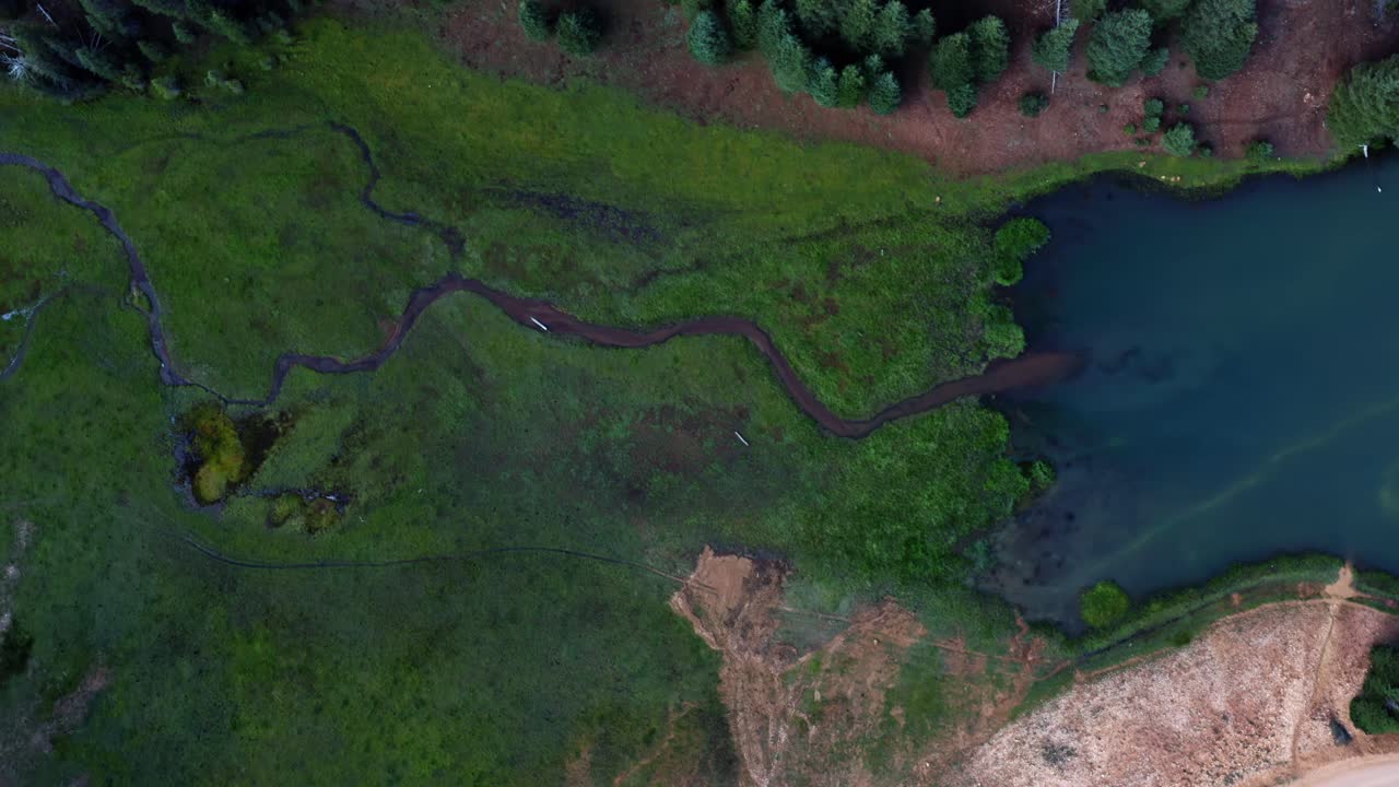 hermoso dron aéreo en la parte superior del ojo de pájaro tiro descendente de un pequeño arroyo rodeado por un campo de hierba que conduce al lago del embalse del prado de anderson hasta el cañón del castor en utah en un cálido día de verano
