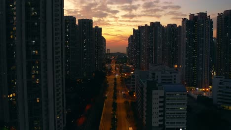 Drone-shot-traveling-backward-above-a-busy-street-in-an-urban-area-full-of-public-housings-buildings-during-sunset