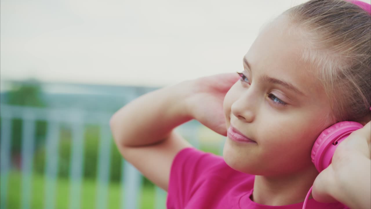 A Young Girl Enjoys Her Music Experience with Bright Pink Headphones, Immersing Herself in the Rhythm While Embracing the Joy of Sound in a Serene Outdoor Setting
