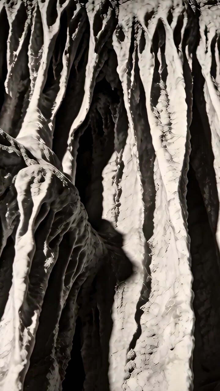 Vertical video: Panning camera revealing calcite drape in cave showing layered texture under light