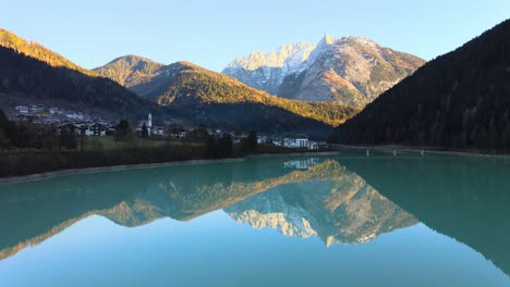 Lago-Con-Agua-Cristalina-Rodeado-De-Montañas-Y-Un-Pequeño-Pueblo-En-Bellluno,-Italia