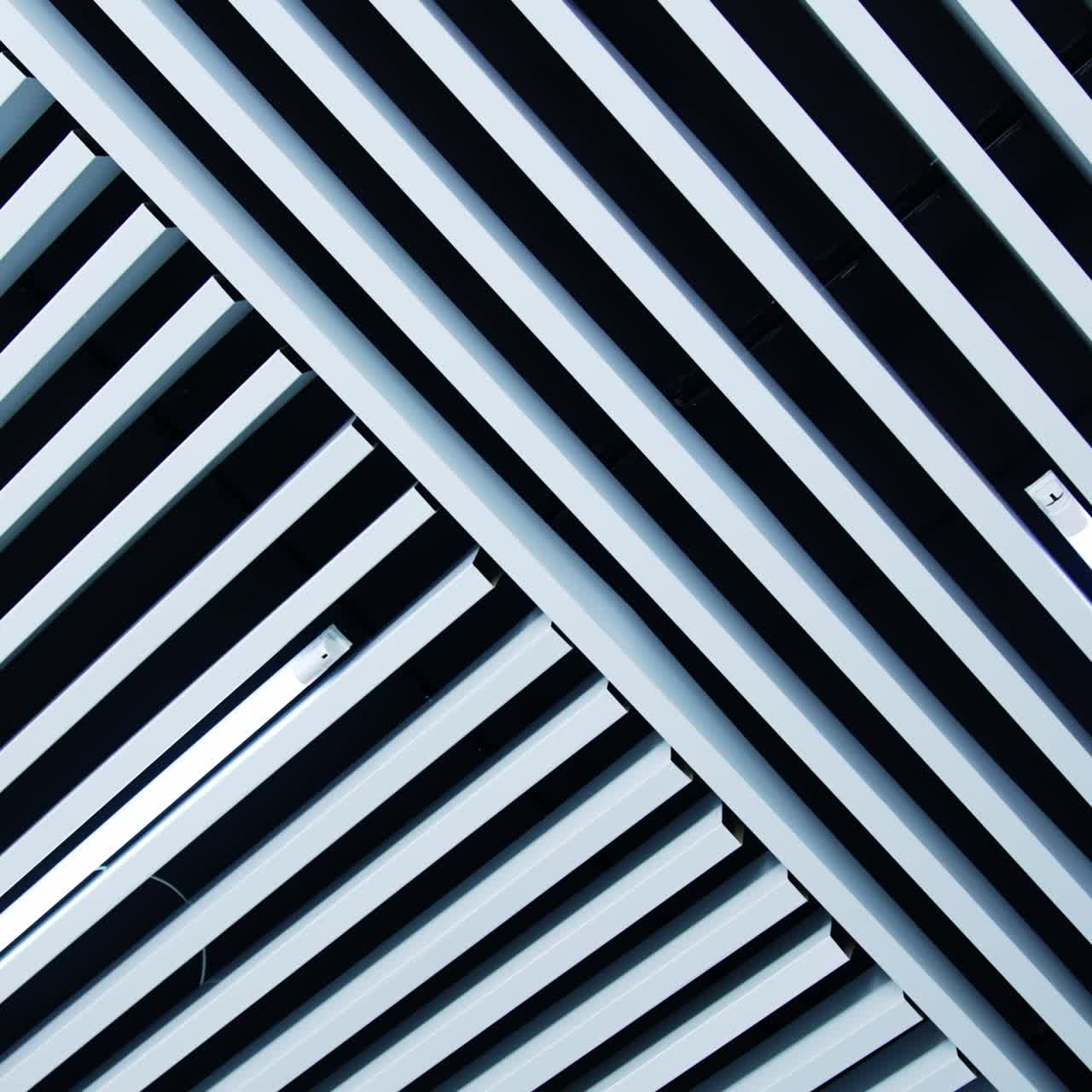 Non-standard decoration of the ceiling with white planks. Long lamps with white light among the ledges. Low angle view