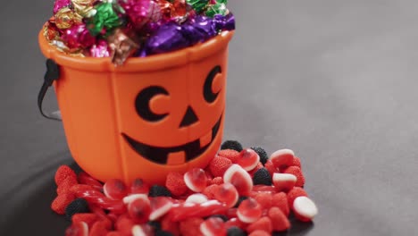 Scary-halloween-pumpkin-printed-bucket-full-of-candies-against-grey-background