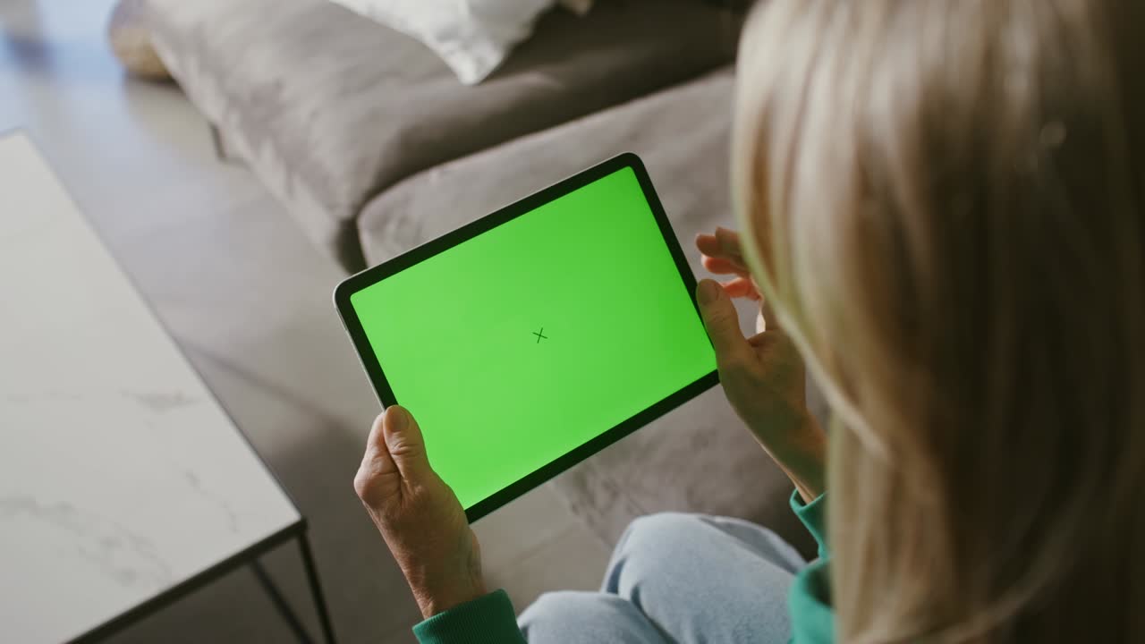 An elderly woman uses a tablet with a green screen, holding it in front of her