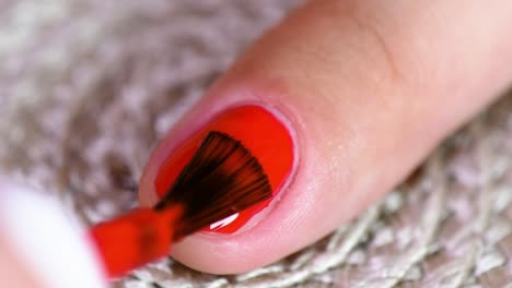 woman applying red nail polish on her index fingernail