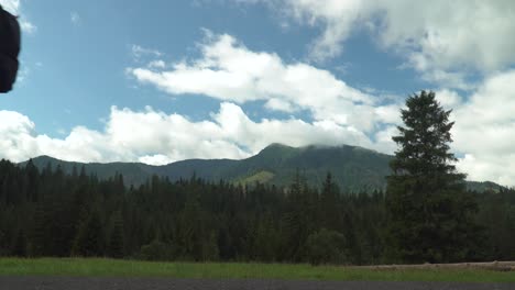 Static-view-over-beautiful-mountains-in-forest-wilderness-in-distance-with-slow-moving-clouds,-male-person-walking-through-frame