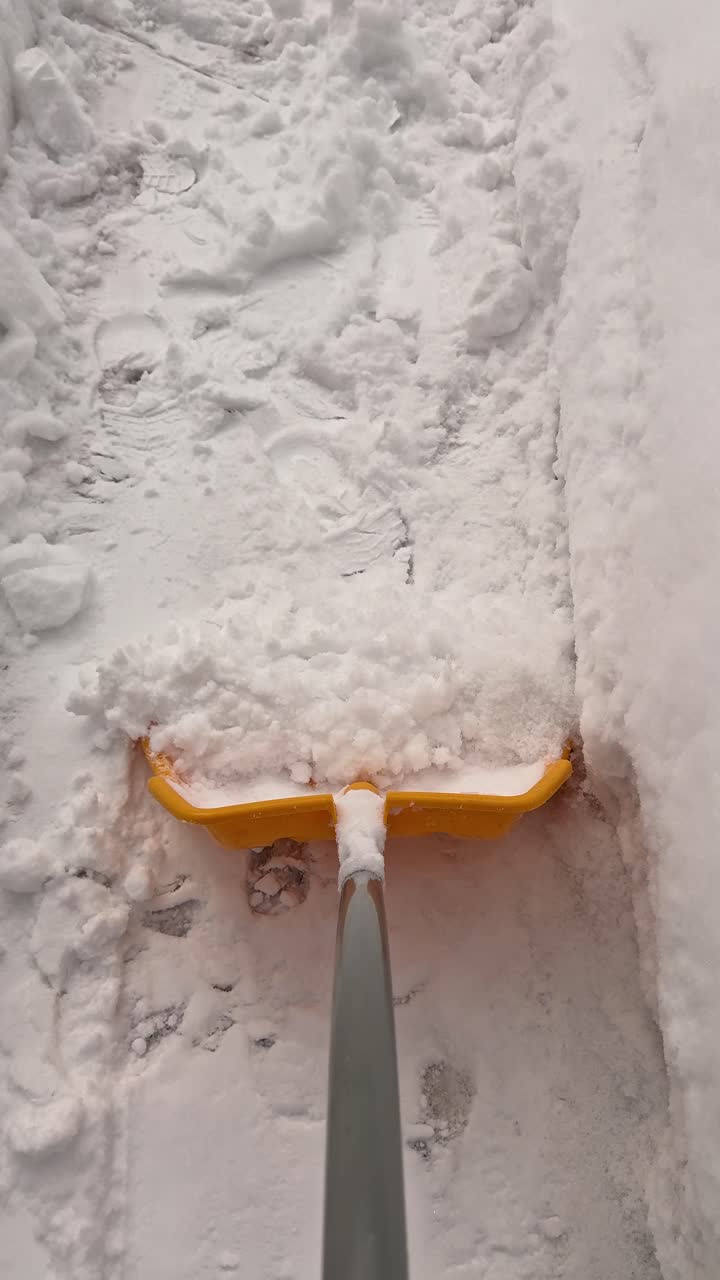 POV pala che termina l'ultima passata su un passaggio pedonale sgomberato, spingendo la neve fresca rimanente verso il bordo del marciapiede. Formato verticale per Reels e Shorts