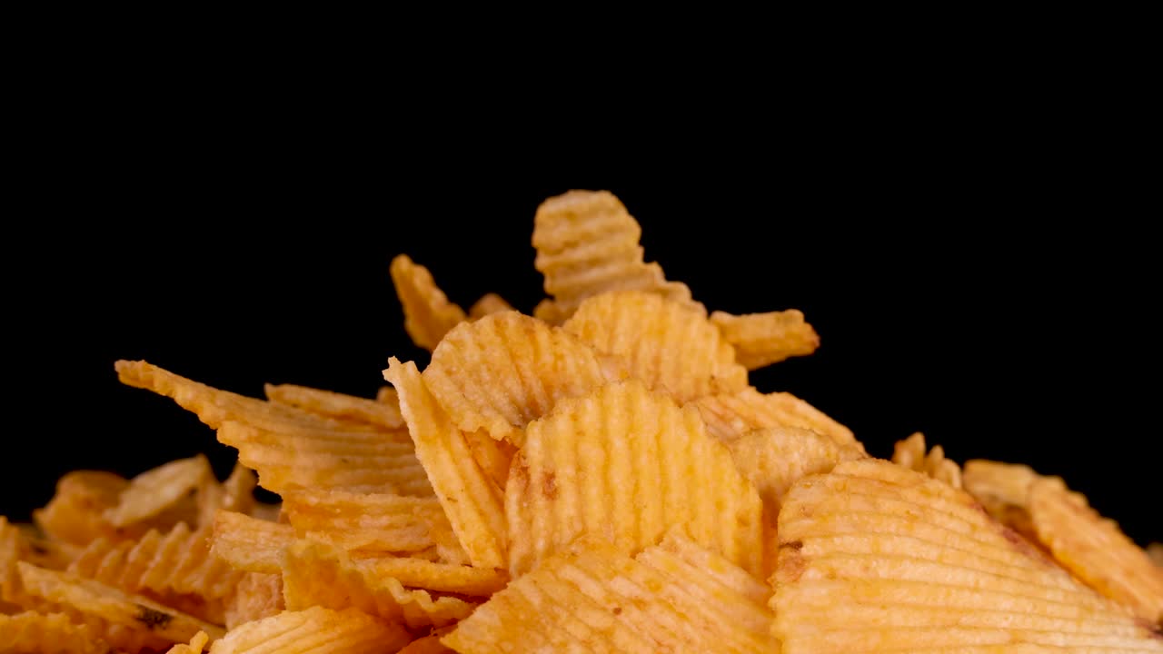 Ludzka ręka wybiera karbowany chips ziemniaczany z dużej sterty, oświetlenie studyjne, czarne tło, zbliżenie