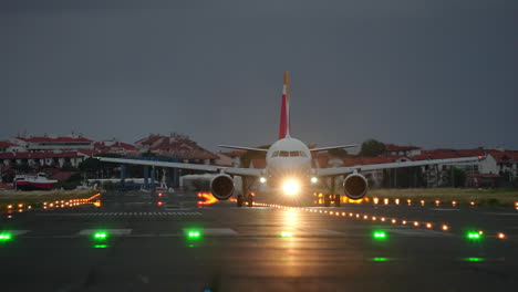 passenger airplane slowly taxiing along runway with navigation lights on during cloudy evening