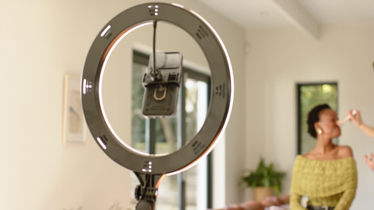 Makeup artist applying blush on African American woman in studio with ring light, copy space