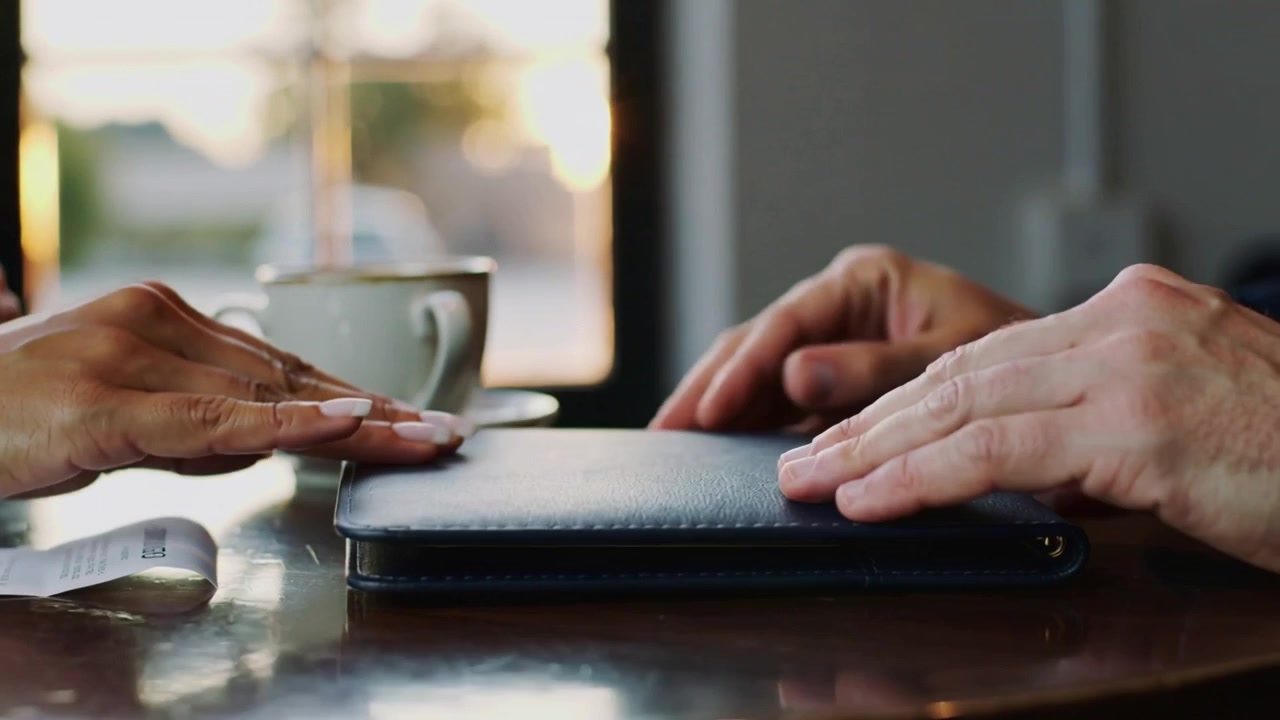 Receiving bill, left hand placing receipt into leather bill holder on cafe table, settling payment