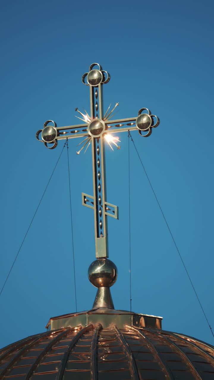 Elegant metallic church cross glowing under clear blue sky. Vertical