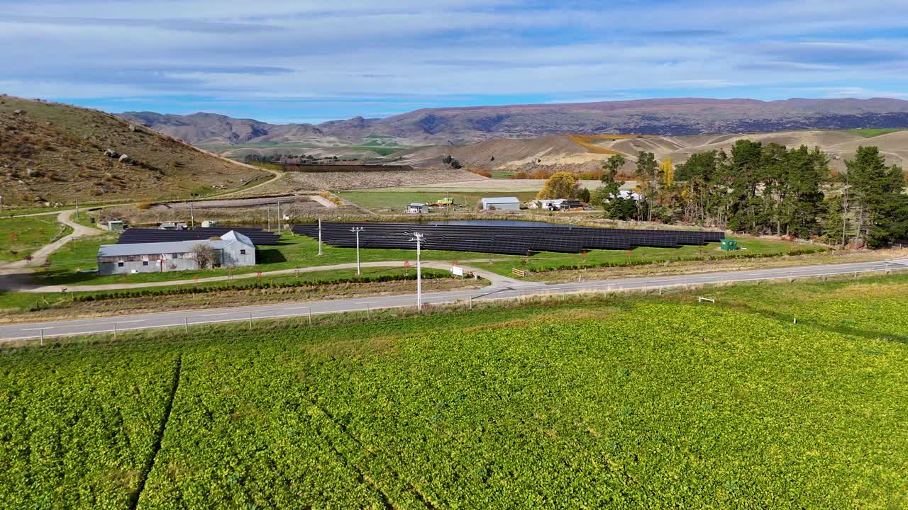 Aerial footage captures a solar farm amidst lush fields and rolling hills in Cromwell, New Zealand, under clear skies