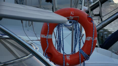 A-close-shot-of-an-orange-life-float-hung-on-a-sports-boat,-swaying-slowly-to-the-rhythm-of-the-waves