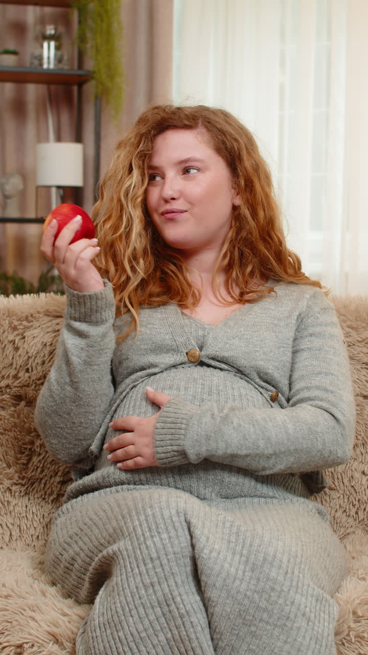 Pregnant woman eating apple gently touching belly relaxed with calm expression and healthy glow