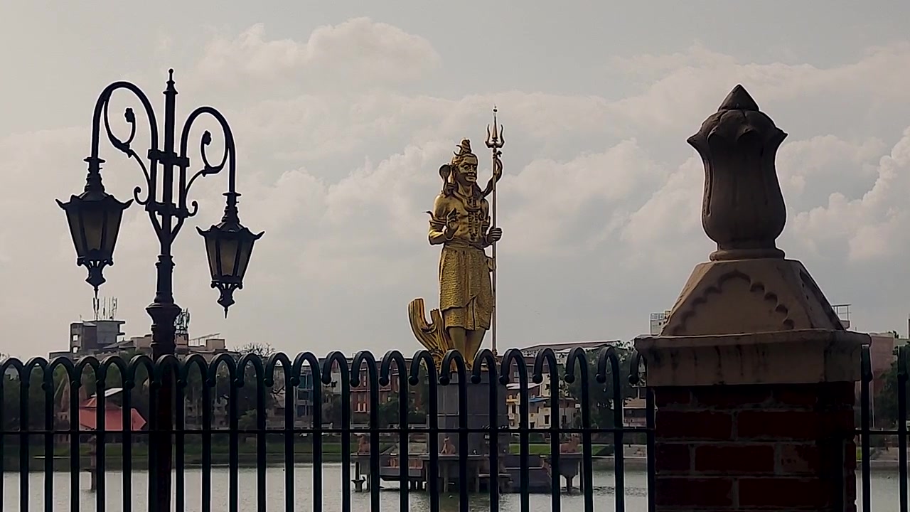 Il lago Sursagar a Vadodara mostra una statua dorata di Shiva incorniciata tra un lampione vintage e un pilastro di un cancello in pietra, punto di riferimento del Gujarat, India