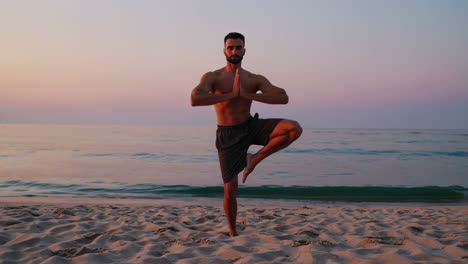 man practicing yoga on a beach at sunset