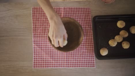 person carefully places freshly baked chipa bread in a rustic wooden bowl on a red checkered cloth, showcasing south american culinary tradition of northeast riverside argentinian provinces