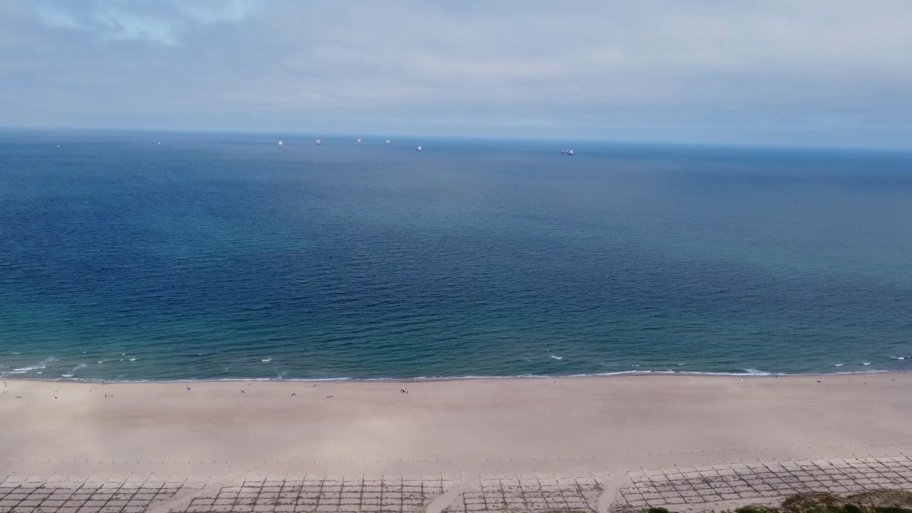 Video udara 4K ketinggian tinggi yang melacak secara lateral di atas pantai berpasir yang indah dan Laut Mediterania. Menampilkan nuansa air biru tua hingga toska, perahu layar di kejauhan, dan garis cakrawala yang jelas