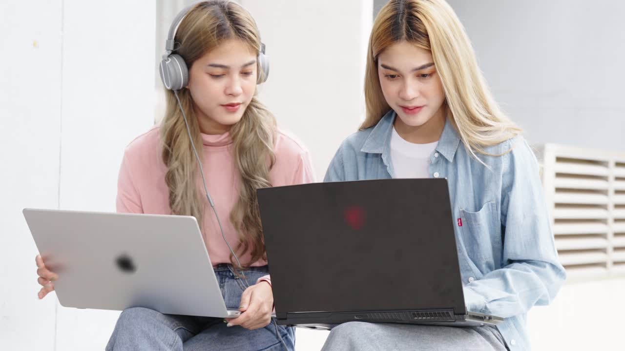Two Asian girls student partners are working on a laptop help study together