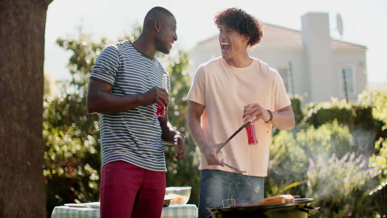 Grilling food, two multiracial male friends smiling and enjoying drinks at outdoor barbecue