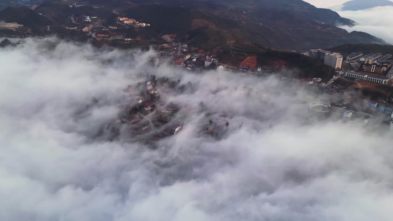 Riprese con drone filmate sopra le nuvole all'alba, inversione di nuvole a Sapa che mostra un insediamento montano con case che emergono attraverso una fitta nebbia negli altipiani del Vietnam settentrionale.